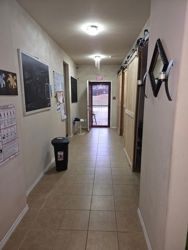 hallway featuring a barn door, mail area, baseboards, and tile patterned floors