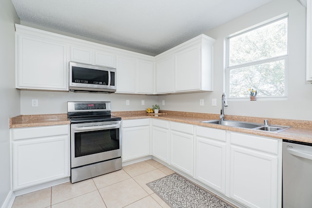 kitchen with light tile patterned floors, stainless steel appliances, light countertops, white cabinetry, and a sink