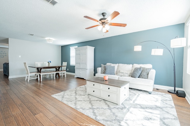 living area with a textured ceiling, wood finished floors, visible vents, a ceiling fan, and baseboards