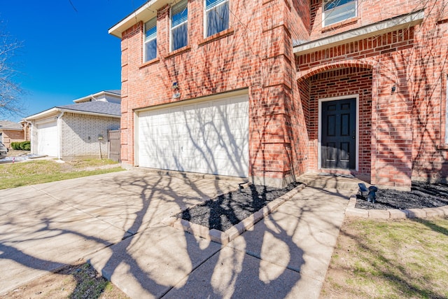 property entrance featuring a garage, concrete driveway, and brick siding