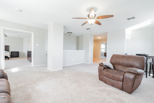 living area with light carpet, ceiling fan, visible vents, and baseboards