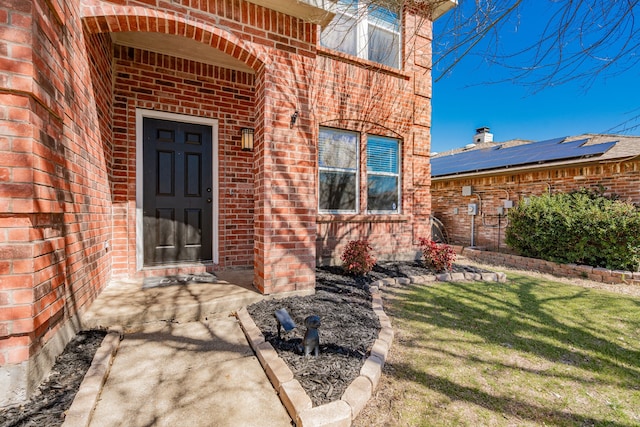 doorway to property featuring a lawn and brick siding