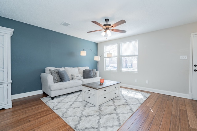 living room featuring visible vents, wood-type flooring, a ceiling fan, and baseboards