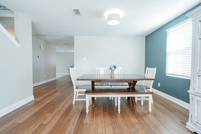 dining space featuring visible vents, light wood-style flooring, baseboards, and a textured ceiling