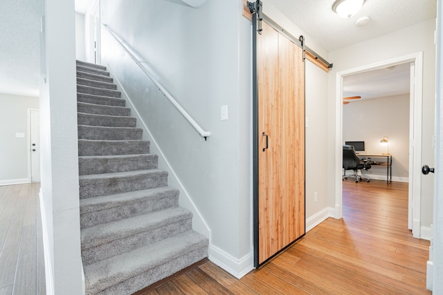 stairs featuring a barn door, baseboards, and wood-type flooring