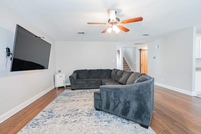 living room with ceiling fan, a textured ceiling, wood finished floors, visible vents, and baseboards