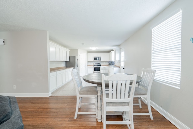 dining space featuring a textured ceiling, light wood-style flooring, and baseboards