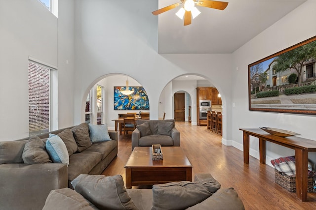 living room featuring baseboards, arched walkways, ceiling fan, wood finished floors, and a high ceiling