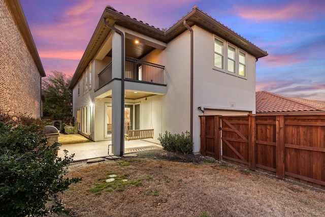 back of house with stucco siding, a patio area, fence, a balcony, and a garage