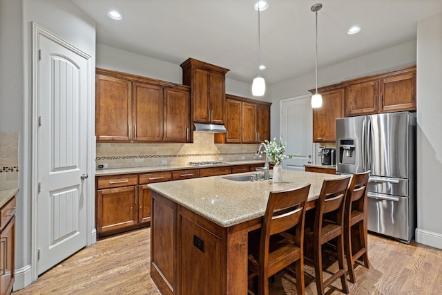 kitchen with stainless steel appliances, light wood-style flooring, a kitchen island with sink, a sink, and under cabinet range hood