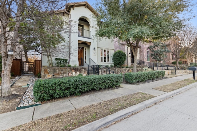 view of front of property with a balcony, a fenced front yard, a tiled roof, a gate, and stucco siding