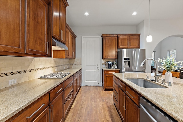 kitchen with light wood finished floors, light stone countertops, stainless steel appliances, under cabinet range hood, and a sink