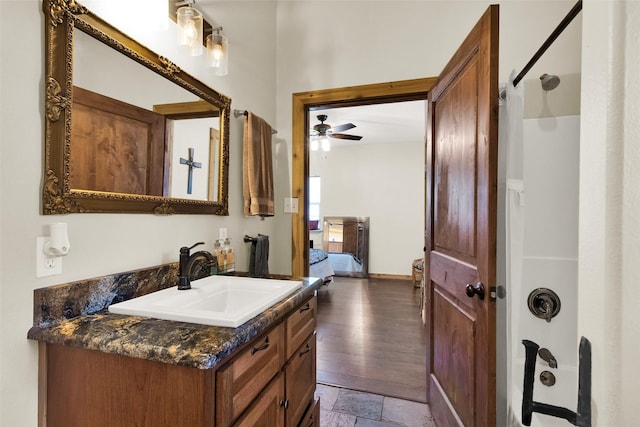 full bathroom featuring baseboards, a shower, ceiling fan, stone tile flooring, and vanity