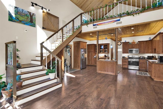 kitchen with a towering ceiling, wood ceiling, appliances with stainless steel finishes, dark wood-type flooring, and a center island