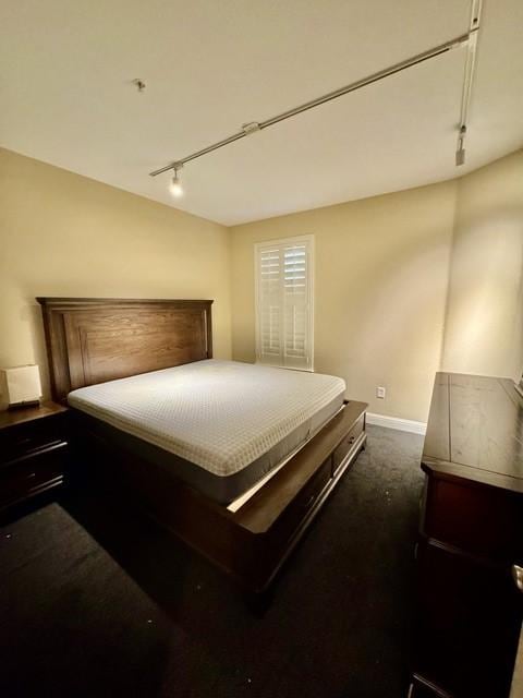 bedroom with dark colored carpet, baseboards, and track lighting
