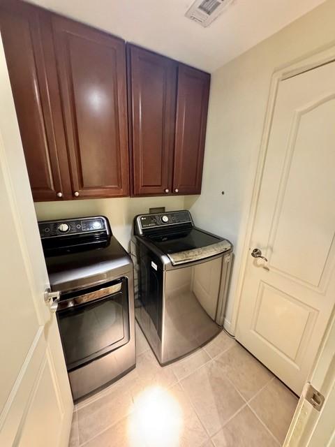 laundry area with visible vents, light tile patterned floors, independent washer and dryer, and cabinet space