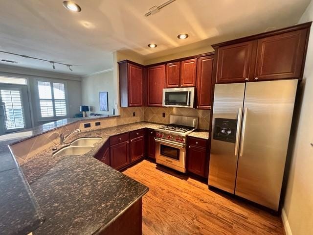 kitchen with stainless steel appliances, tasteful backsplash, a sink, dark stone countertops, and a peninsula