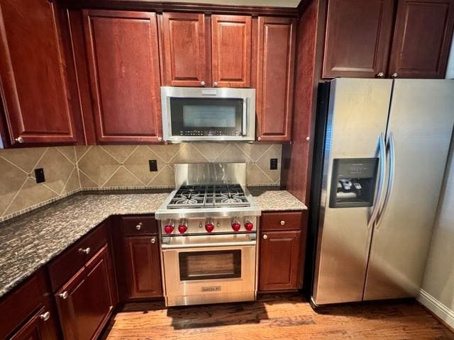 kitchen featuring decorative backsplash, appliances with stainless steel finishes, stone countertops, light wood-style floors, and dark brown cabinets