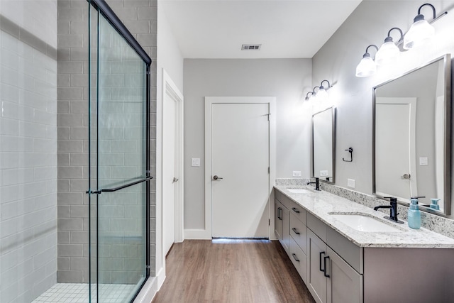 full bath with double vanity, a shower stall, a sink, and wood finished floors