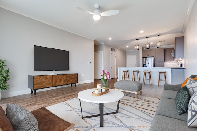 living room with a ceiling fan, baseboards, visible vents, light wood-style floors, and ornamental molding