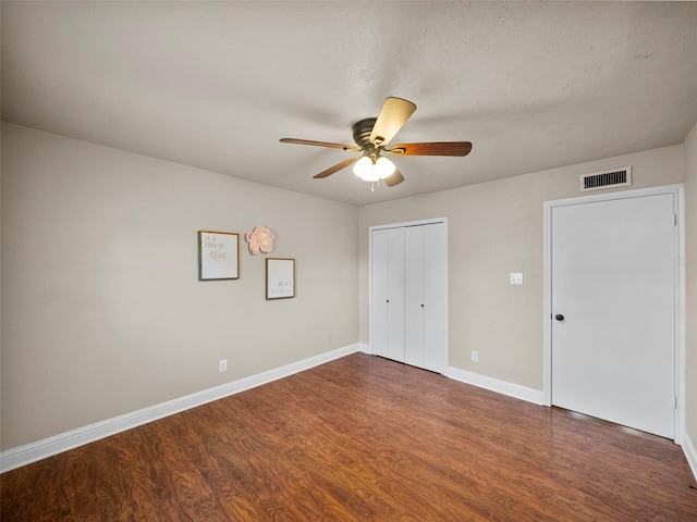 unfurnished bedroom with ceiling fan, visible vents, baseboards, a closet, and dark wood finished floors