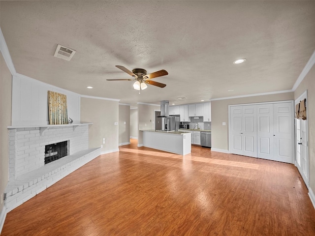 unfurnished living room featuring a brick fireplace, light wood-style flooring, visible vents, and ornamental molding