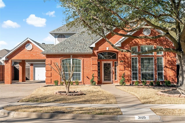 traditional home featuring roof with shingles, driveway, brick siding, and an attached garage