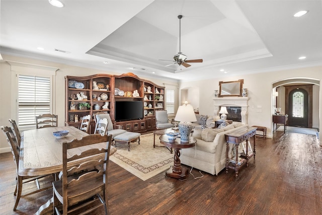 living area featuring arched walkways, a raised ceiling, dark wood-type flooring, and a glass covered fireplace