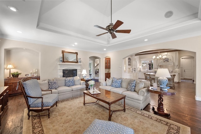 living room with arched walkways, ornamental molding, wood finished floors, a tray ceiling, and recessed lighting