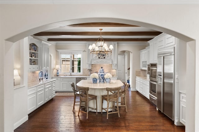 dining room with arched walkways, ornamental molding, dark wood-type flooring, a chandelier, and beam ceiling