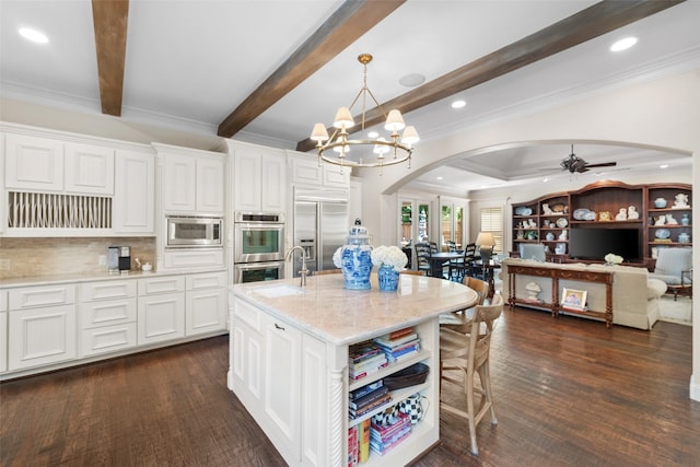 kitchen featuring built in appliances, arched walkways, ceiling fan with notable chandelier, dark wood-style flooring, and white cabinetry