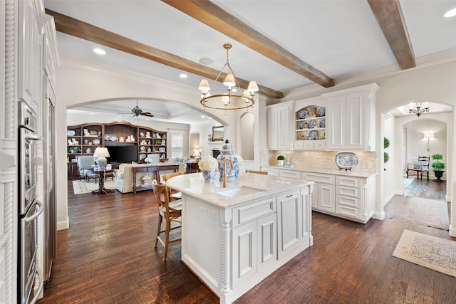 kitchen featuring arched walkways, open floor plan, white cabinetry, and dark wood-style flooring