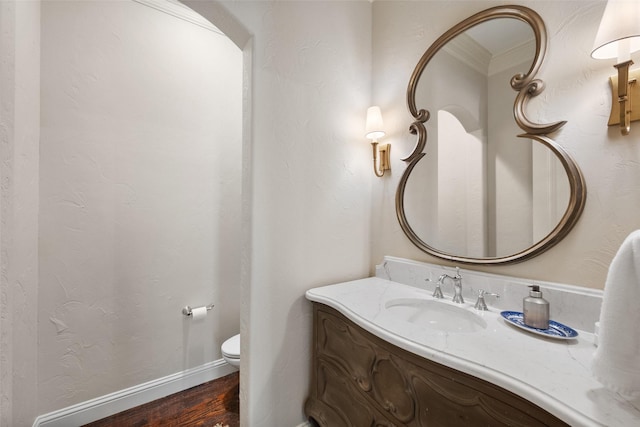 half bath with a textured wall, toilet, wood finished floors, vanity, and baseboards