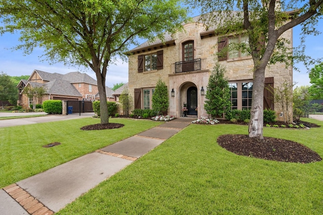 view of front of home featuring a front yard, a balcony, stone siding, and concrete driveway
