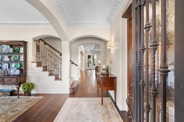 entrance foyer featuring arched walkways, wood finished floors, stairs, crown molding, and a decorative wall