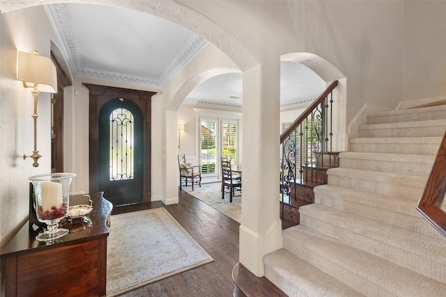 entrance foyer featuring arched walkways, stairway, wood finished floors, and crown molding