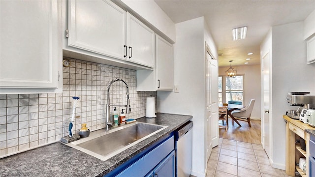 kitchen featuring dark countertops, blue cabinets, stainless steel dishwasher, white cabinetry, and a sink