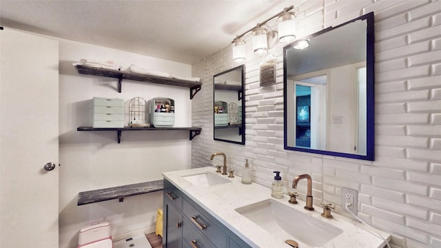 full bath with a textured ceiling, double vanity, tasteful backsplash, and a sink