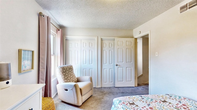 bedroom featuring visible vents, light carpet, a textured ceiling, and two closets