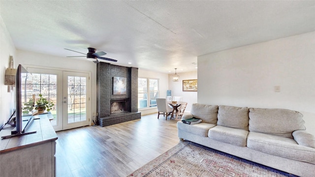 living area with ceiling fan, wood finished floors, a textured ceiling, french doors, and a fireplace