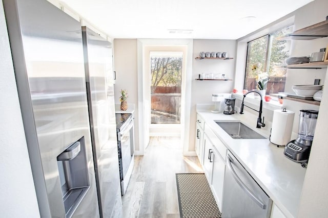 kitchen with open shelves, light countertops, appliances with stainless steel finishes, a sink, and light wood-type flooring