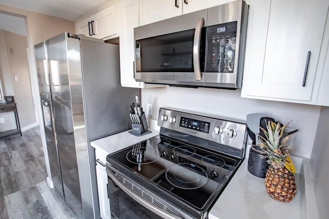 kitchen with light stone countertops, white cabinetry, stainless steel appliances, and wood finished floors