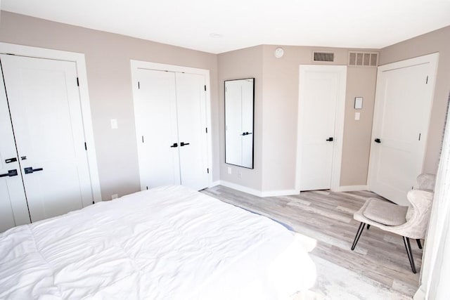 bedroom with light wood-type flooring, baseboards, visible vents, and multiple closets