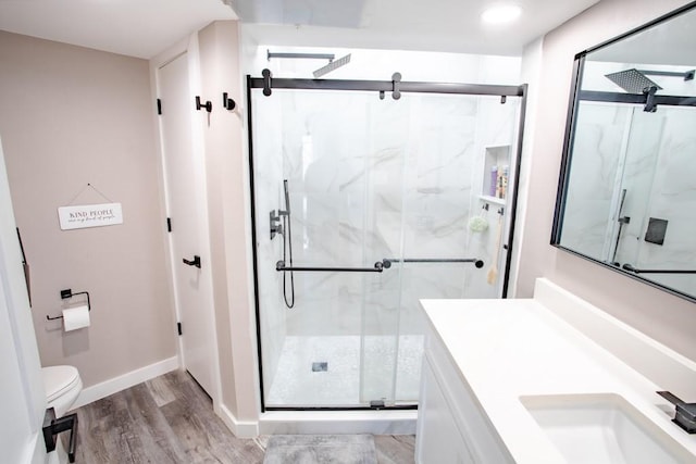 full bath with a marble finish shower, baseboards, toilet, wood finished floors, and vanity