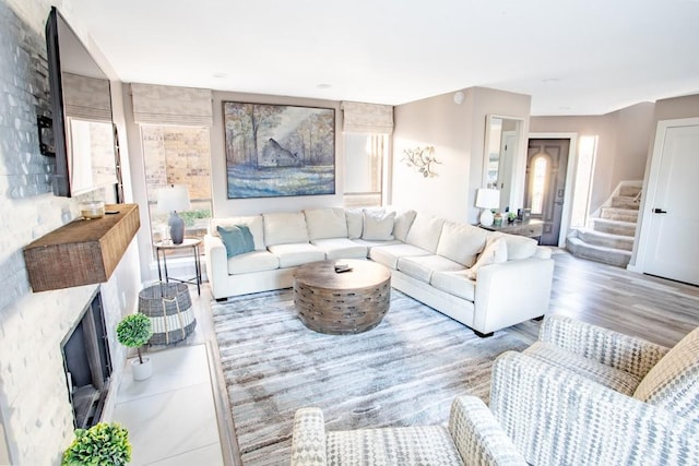 living room featuring plenty of natural light, a fireplace, stairway, and wood finished floors