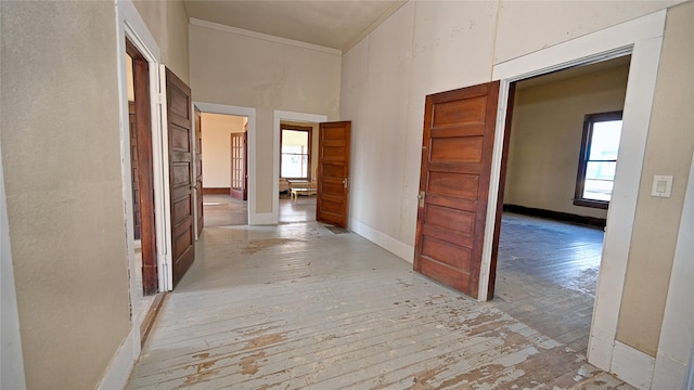 corridor with ornamental molding, light wood finished floors, a towering ceiling, and baseboards