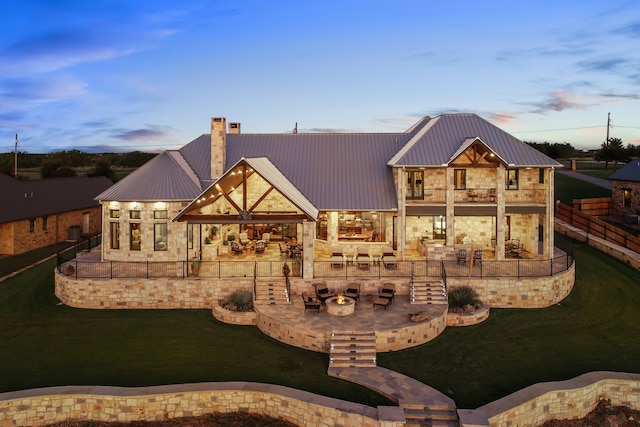 back of house at dusk featuring a balcony, stone siding, a patio area, and metal roof