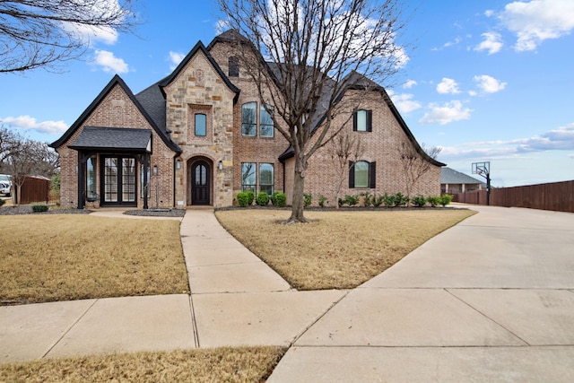 french country style house featuring french doors, brick siding, fence, stone siding, and a front lawn