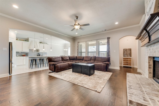 living room with baseboards, arched walkways, dark wood-style floors, ornamental molding, and a brick fireplace