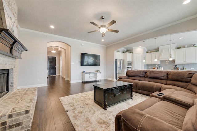 living room featuring arched walkways, a brick fireplace, crown molding, and wood-type flooring